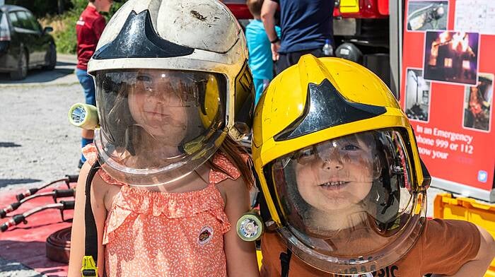 Schull, West Cork, Ireland. 28th Jul, 2024. The sun shone for Schull Agricultural Show today. Hundreds of people attended to watch many horse classes. Trying on firefighter's helmets for size were Saoirse & Fionn Hayes from Schull. Picture: Andy Gibson.