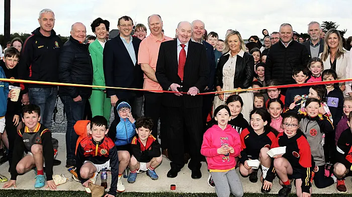Newcestown GAA club president Seán Crowley surrounded by his club officers, invited guests and the future generation of players, cutting the tape to officially open the new Astroturf sports complex and second pitch, Páirc Uí Mhathúna,  last Saturday evening.   (Photo: Paddy Feen)