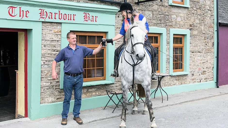Publican Frank Walsh serves a pint of creamy stout to his first customer in six months, Imogen Bertin and her horse 
Hatbox when they called to the Harbour Bar in Robert’s Cove. (Photo: David Creedon / Anzenberger)