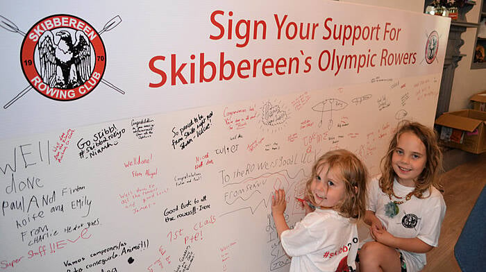 Millie and Lara Dempsey signing their names on the huge poster at the pop-up shop. (Photo: Anne Minihane)