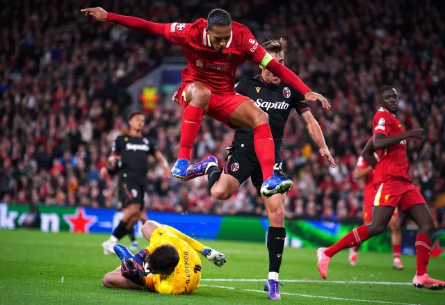 Virgil van Dijk hurdles over his goalkeeper as Alisson Becker slides to pick up the ball